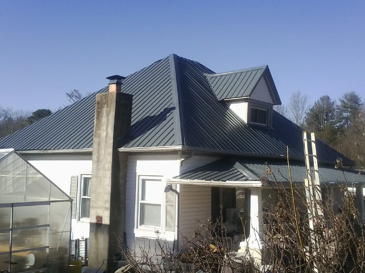 Dark blue standing seam metal roof on a white farmhouse with dormer — Slate & Tile Roof Repair by Roofing Brothers in Ardenvoir