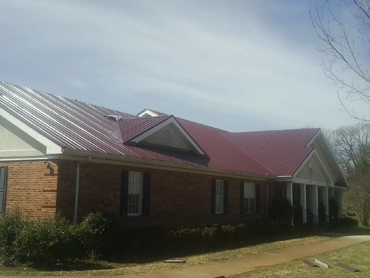 Red metal roof with gabled entries on a long brick building, from a Hail Damage Roof Repair job in Ardenvoir