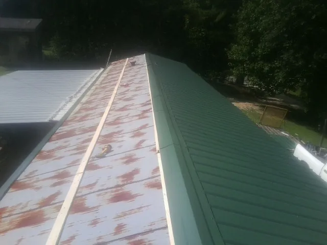 Old rusted panels beside newly installed green metal roofing — Wind Damage Roof Repair by Roofing Brothers in Ardenvoir