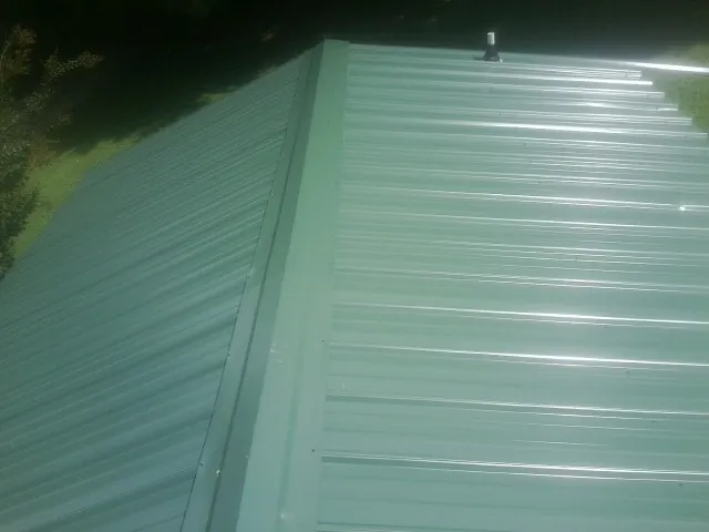 New green metal panels meeting at the ridge of a roof — Flat Roof Repair work by our crew in Ardenvoir