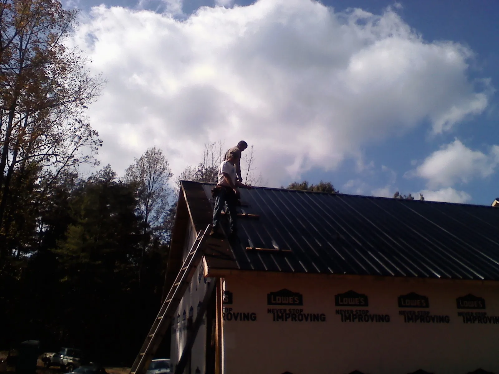 Roofer fastening dark metal panels high against a cloudy sky, from a Roof Inspection job in Ardenvoir
