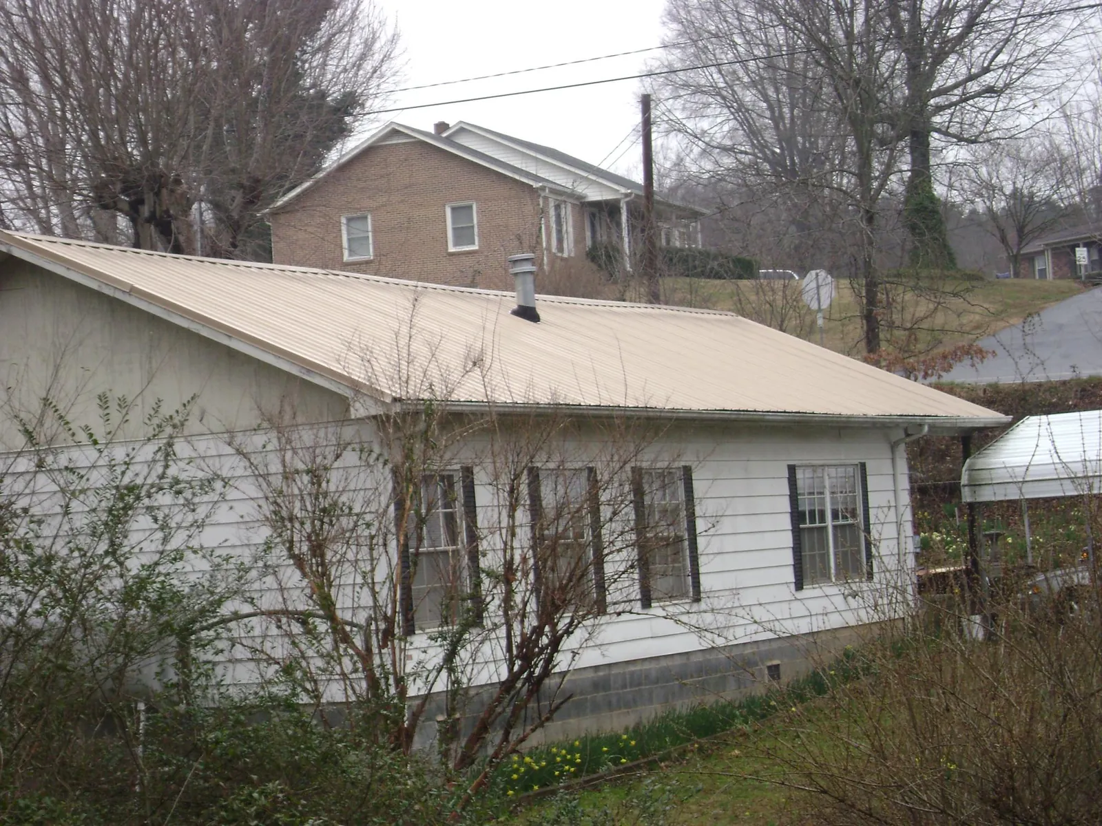 Tan metal roof on a white sided house set into a hillside — Commercial Roofing by Roofing Brothers in Ardenvoir