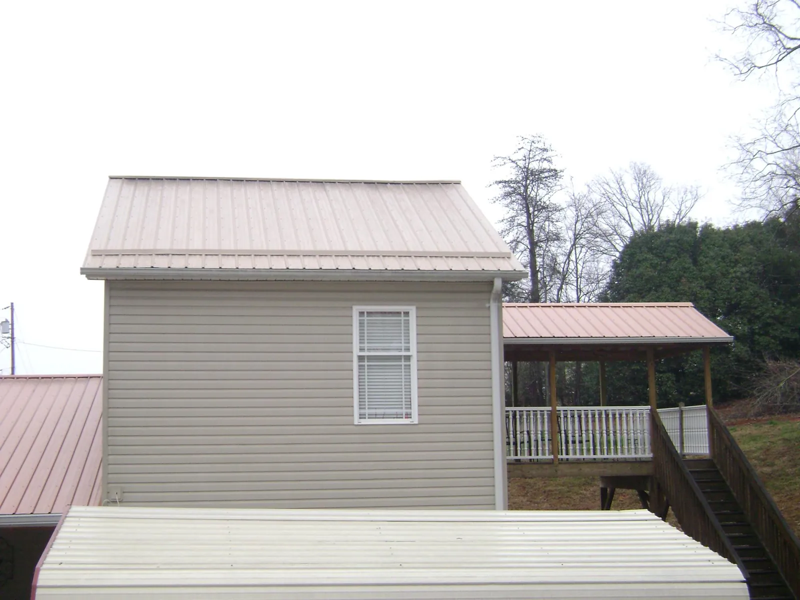 Tan metal roofs on a two story addition and attached porch, from a Roof Replacement job in Ardenvoir